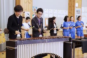 サンバのリズムを刻む児童たちと演奏を楽しむ前田さん(左)と藤原さん(左から3人目)