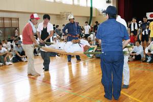 体育館では竹と毛布を使った即席担架を実践したほか、毛布がないときは厚手の上着を使う方法も説明