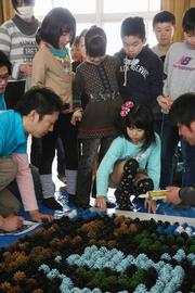 縦180cm×横360cmのパネルにペンキで塗装した松ぼっくりをはり、絵を完成させていく児童たち