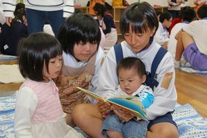 赤ちゃんに絵本を読み聞かせてあげる生徒ら。じっとして聞いていてくれるかな!?