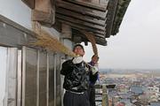 時折小雨が降りそそぐ中、竹ぼうきを使って回廊